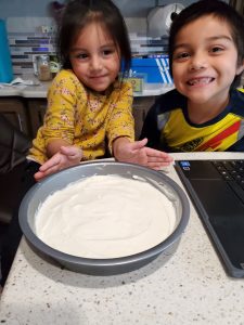 Compass Charter Schools Online Elementary students happy with baking class, presenting cake batter with smiles near a laptop.