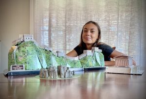 Alt text: Smiling Compass Charter Schools Online student with models of architectural wonders- The Great Wall of China, Stonehenge, and the Parthenon.