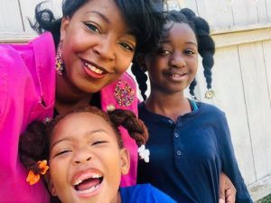 A Compass Online learning coach smiles and embraces her two happy scholars, one middle school age scholar, one elementary school scholar.