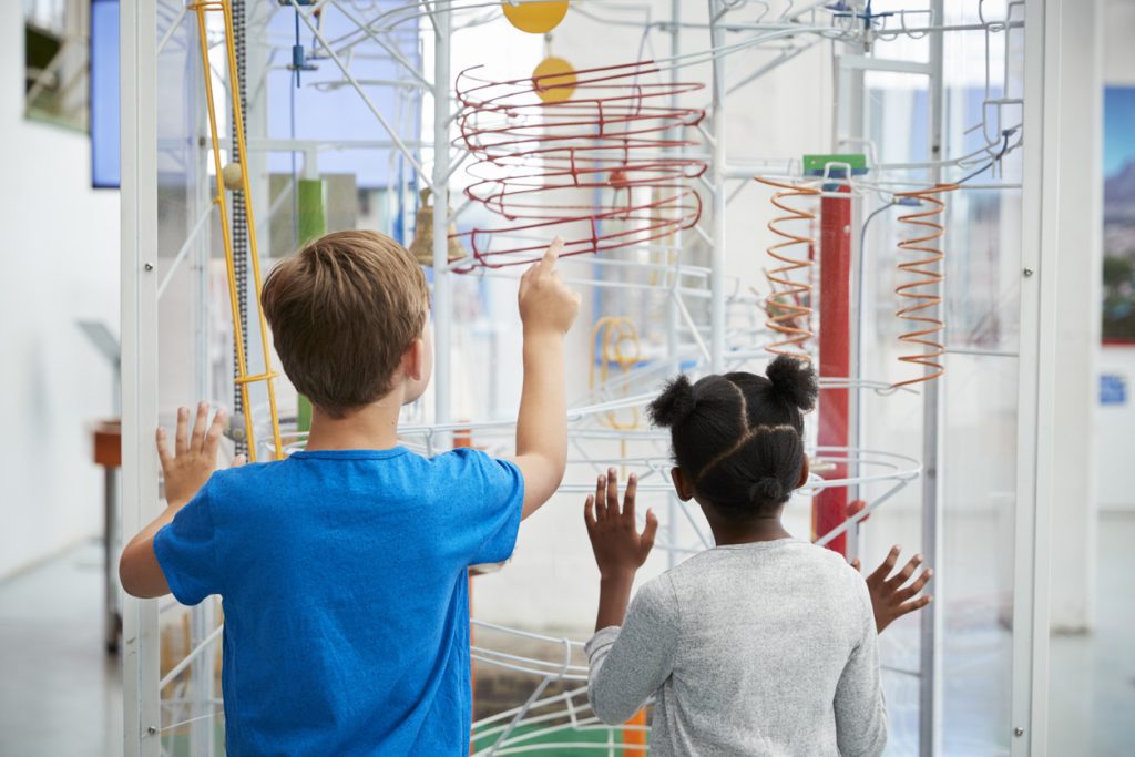 Curious elementary students following a marble in an artful science sculpture designed to display properties of physics in a fun colorful way.