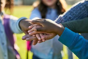 Several children’s hands pile on top of each other in a symbol of togetherness and teamwork.