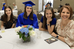 A Compass Charter School senior smiles in her gown and cap, surrounded by a happy family. Compass prepares scholars for lifelong learning