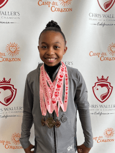 Compass Charter School middle grade scholar poses with a big smile and 4 big medals she won in Camp del Corazon