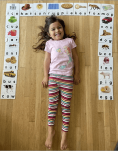 A happy Compass Charter School scholar lies in the middle of her spelling homework with three letter words on cards.
