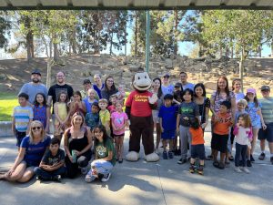 Compass Charter School staff, learning coaches, and scholars pose with Curious George at a field trip in Costa Mesa.
