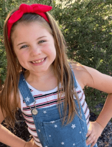 Compass Charter Schools home study scholar wears a red headband and smiles in her own backyard.