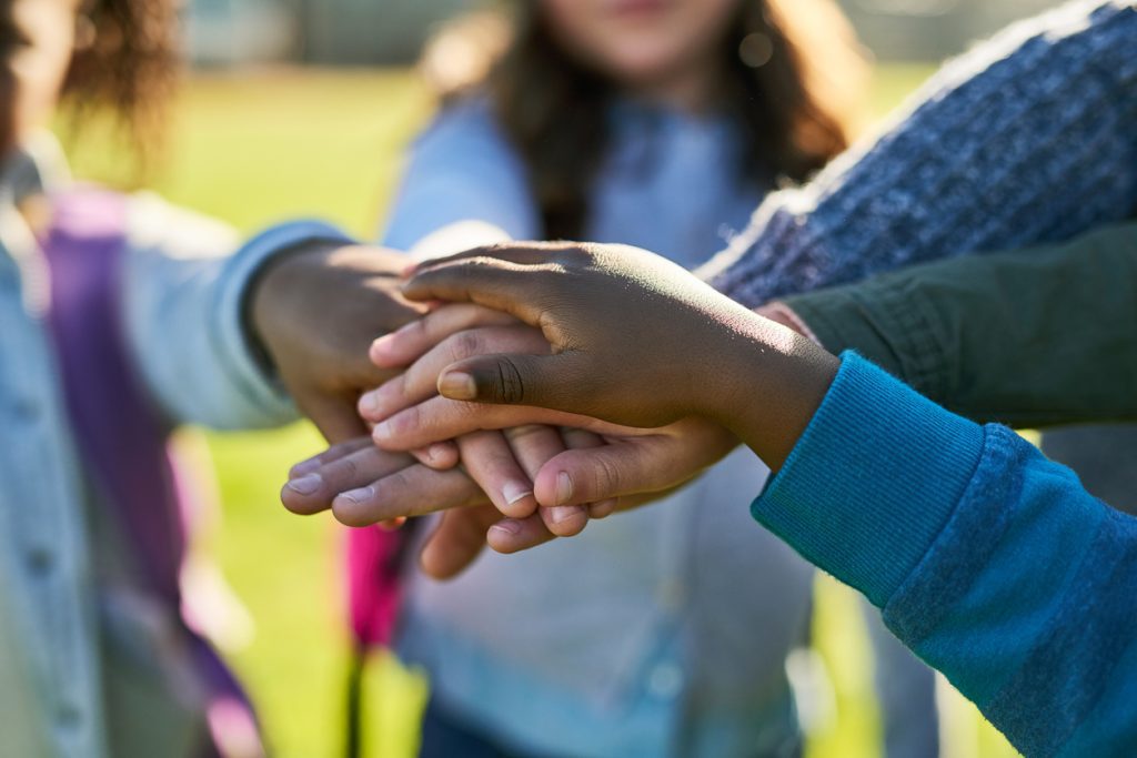 Young scholars stack hands over each other in a symbol of creating safe space for diversity, inclusion, and equity in school.